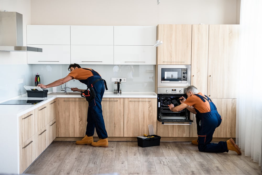 Deux personnes assemblent et ajustent des meubles dans une cuisine.