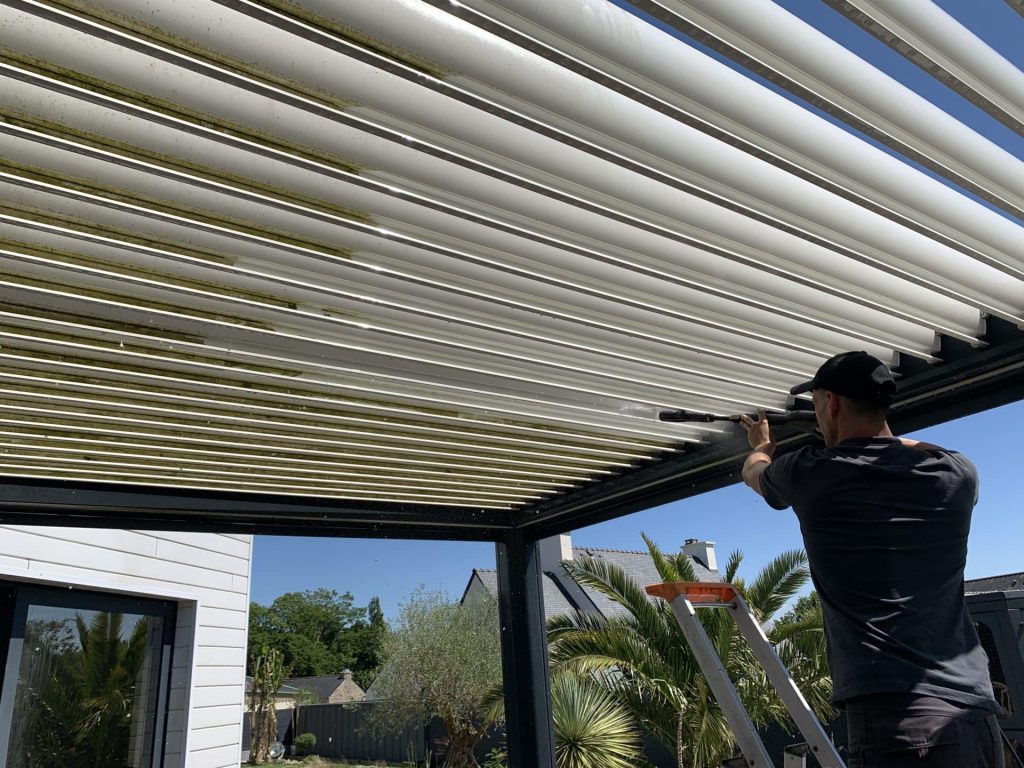 Personne nettoyant la face inférieure des lames d’une pergola bioclimatique.