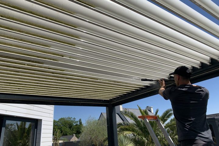 Personne nettoyant la face inférieure des lames d’une pergola bioclimatique.