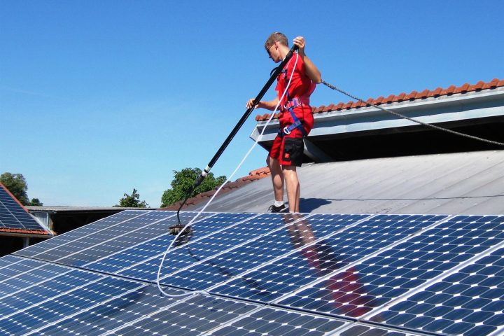 Personne nettoyant des panneaux photovoltaïques en toiture avec une perche.