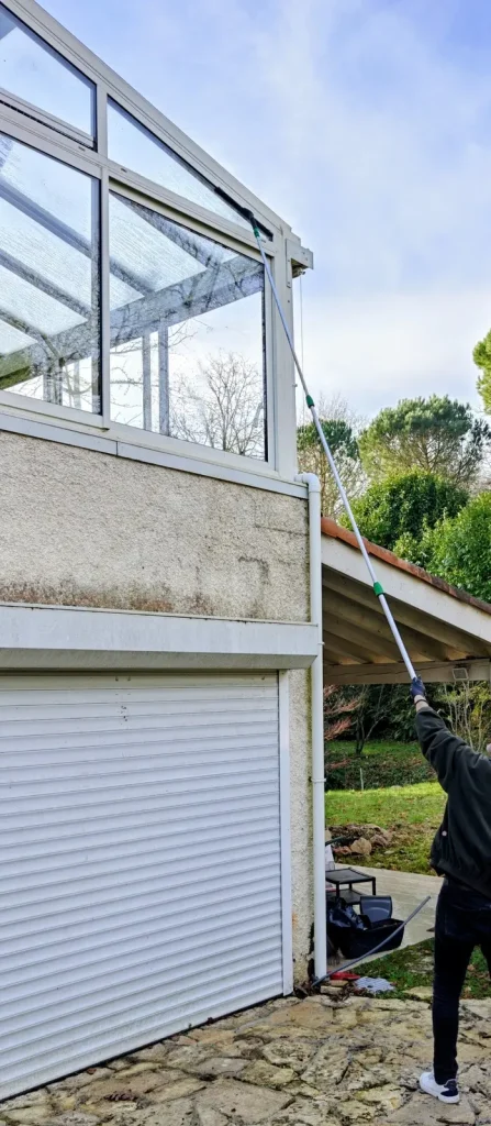 Technicien QUALIFICACE nettoyant les vitrages d’une véranda en hauteur