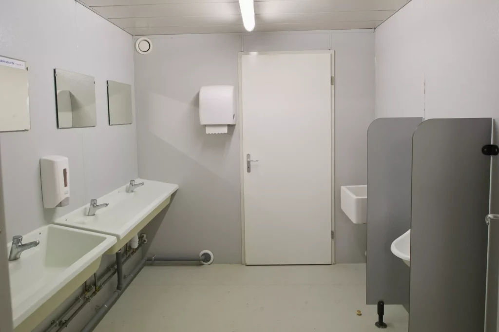 Sanitaires modulaires avec deux lavabos, un miroir et des urinoirs.