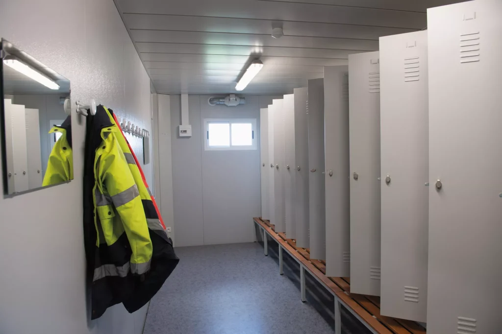 Vestiaire modulaire avec casiers, banc central et vêtements de chantier.